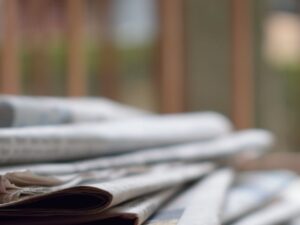 A close-up of a stack of newspapers resting on a desk, symbolizing information and media.