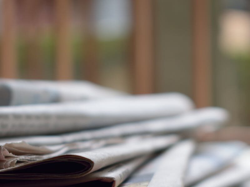A close-up of a stack of newspapers resting on a desk, symbolizing information and media.